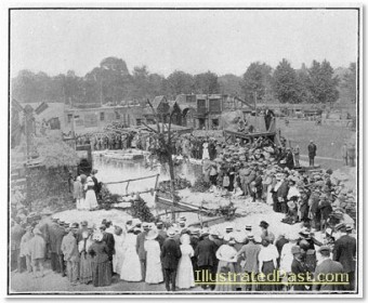 A movie scene being filmed in the open. The cameras and lights are mounted on a platform on the right of the picture. Note the large number of extras.